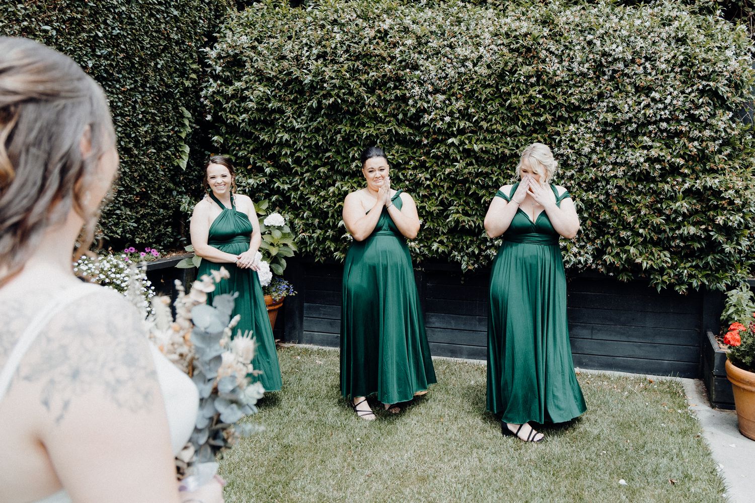 Bridesmaids in emerald green dresses react with joy as they see the bride, captured by Apertured Media Auckland Wedding Photographer.