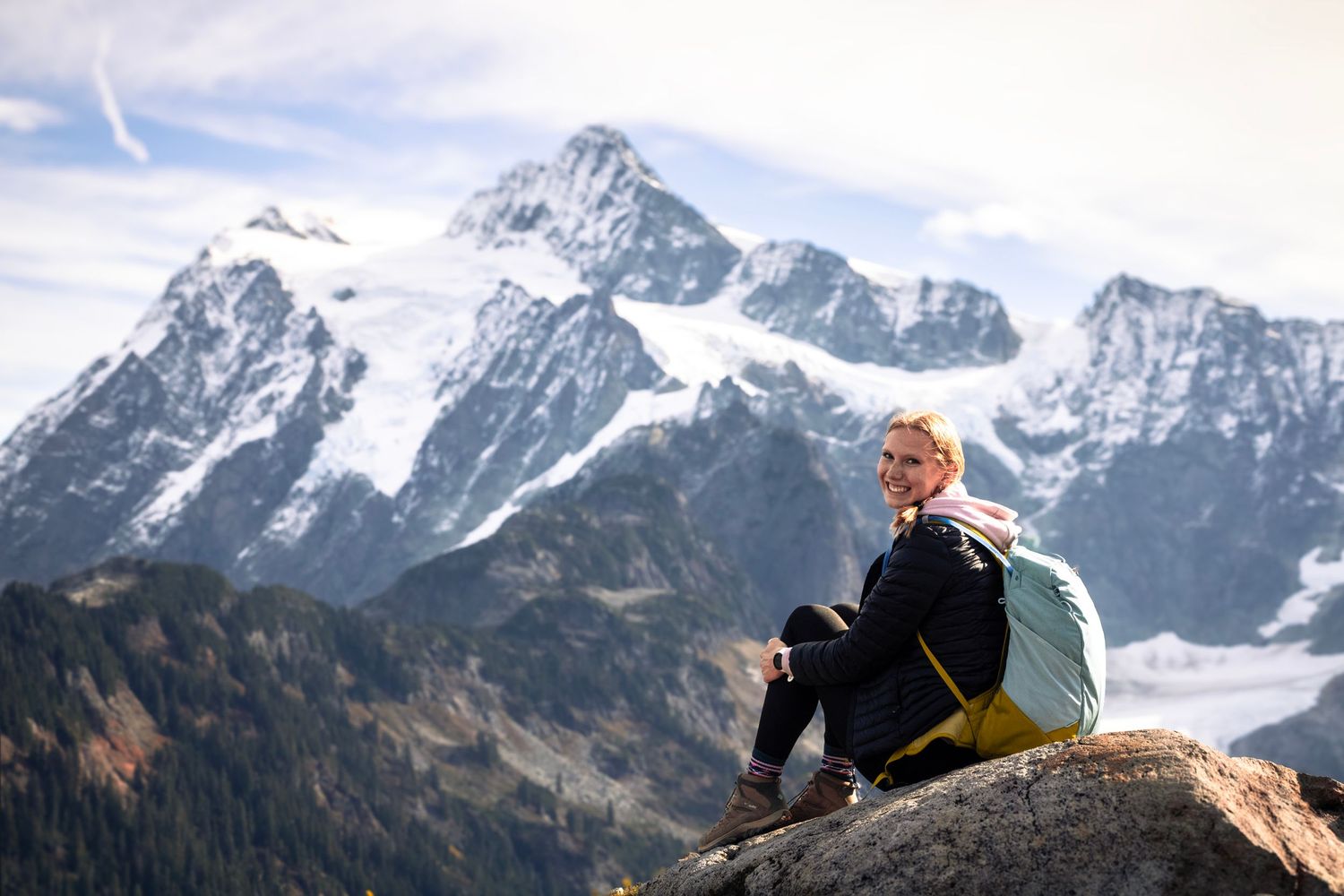 girl sits on rock looking at camera as mountain looms in the distance behind her