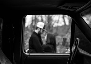 black and white image of blurred couple embracing each other while framed by the window of a truck