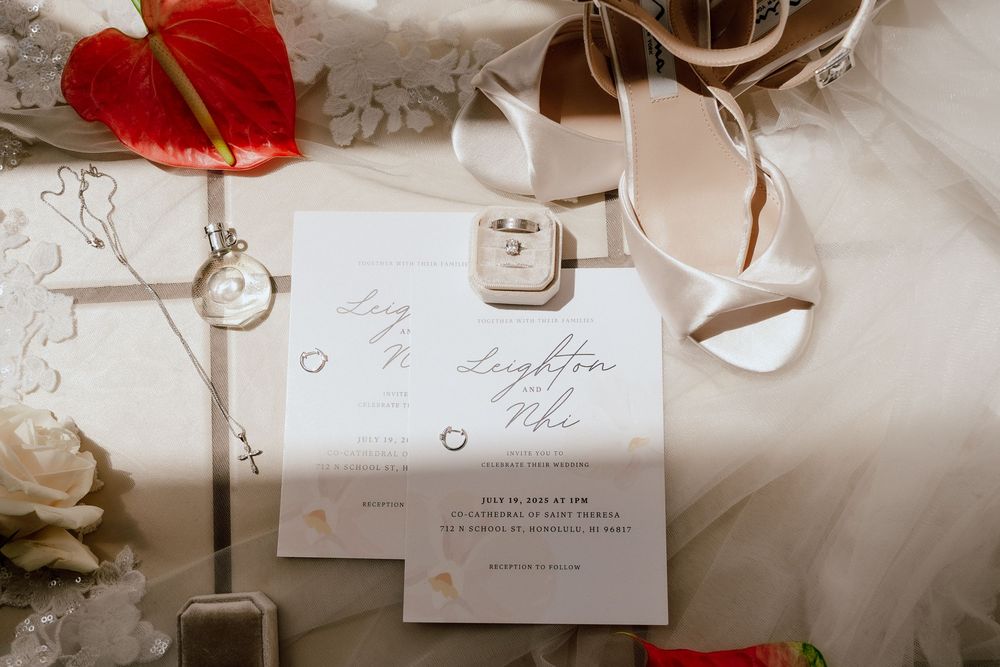 Wedding invitation with white heels, antique key, red heart decoration and white roses on a light fabric background.