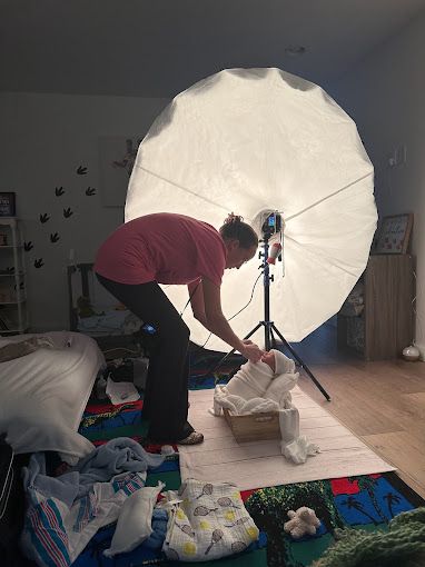 Photographer setting up large white umbrella studio light for newborn photography session indoors.