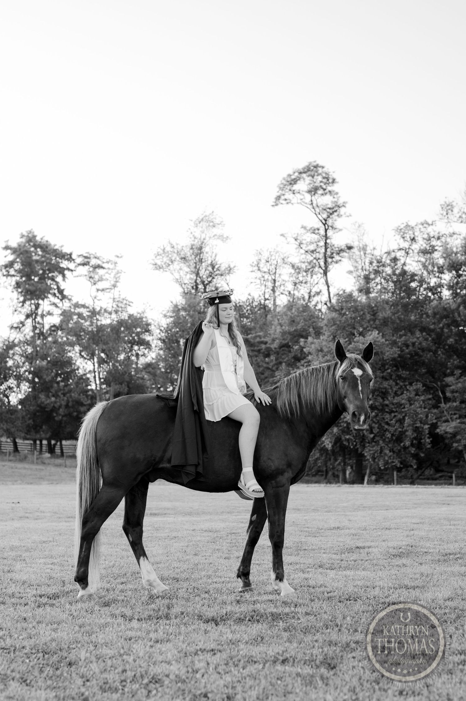 Black and white portrait of a graduate on horseback with trees in the background.
