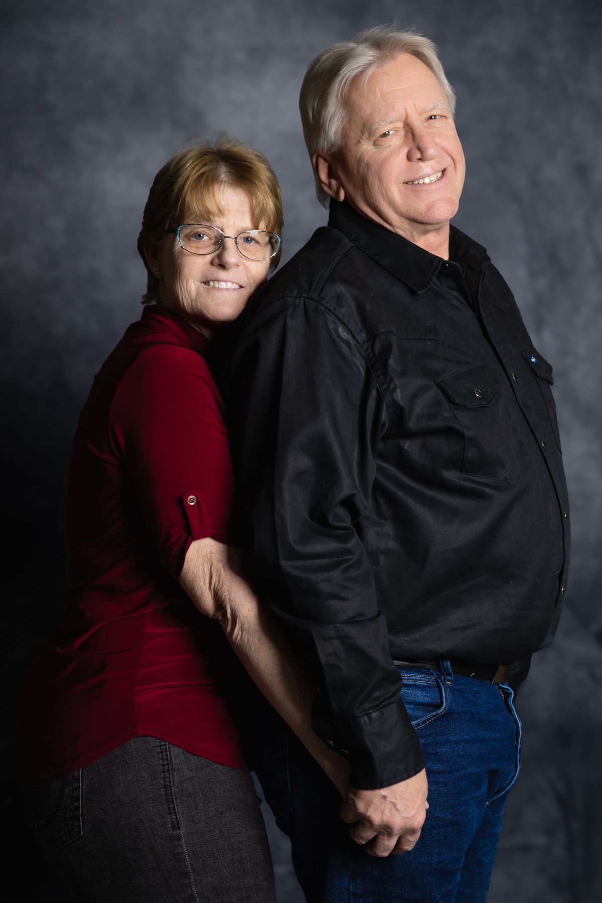 Studio portrait of a couple in casual attire against a dark grey background.