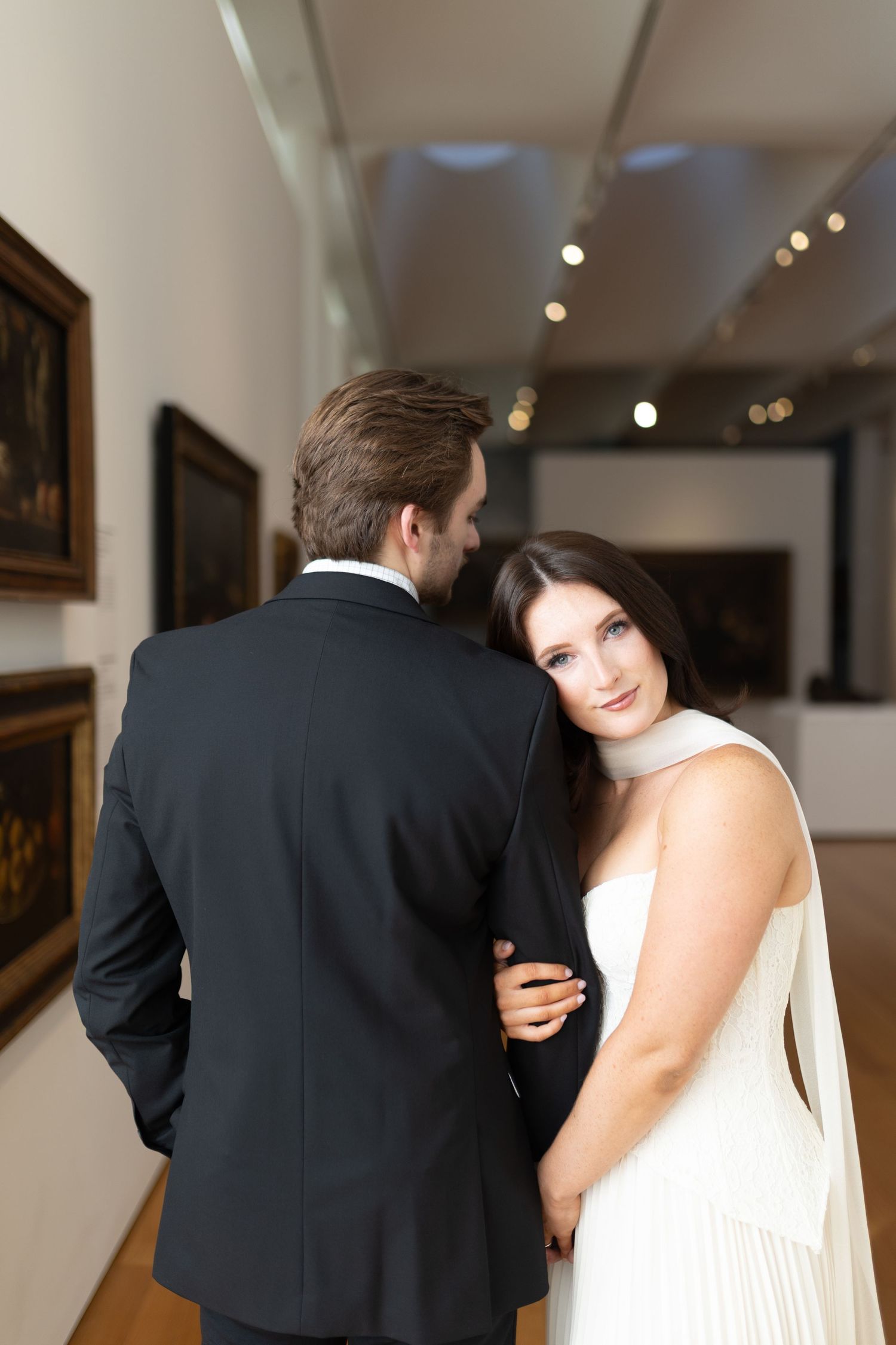 An elegant wedding moment captured in a bright indoor gallery with white walls and spotlights.