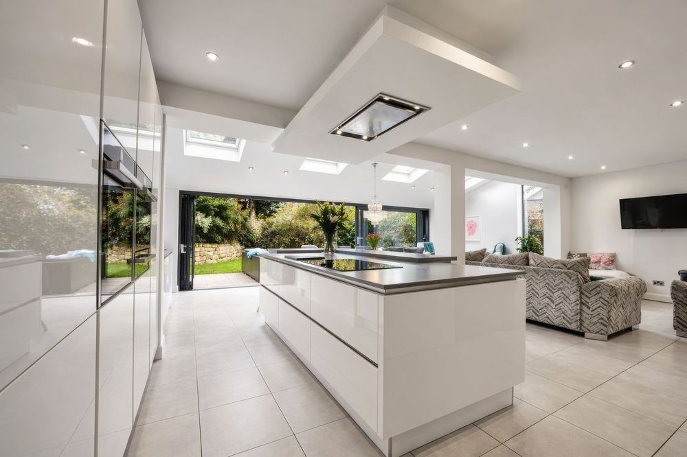 Photography for Modern white kitchen with island, skylights, and bifold doors opening to a garden in a bright open-plan living space.