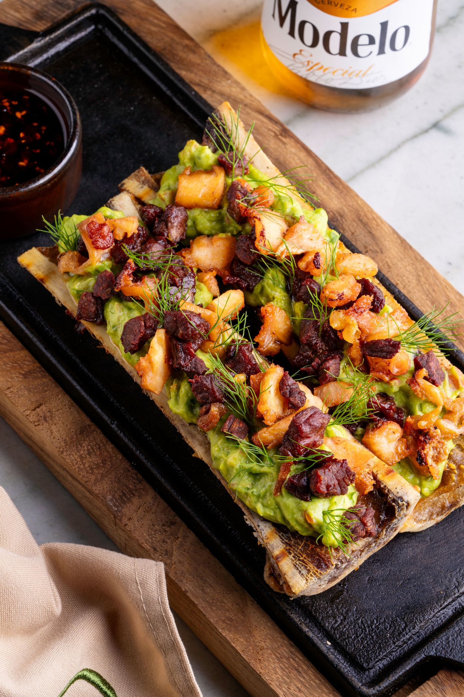 Gourmet open-faced sandwich with grilled meats and vegetables served on a rustic wooden board.