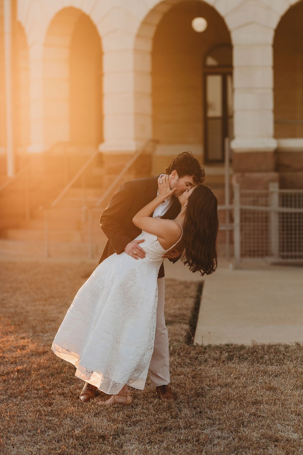 A romantic sunset dance dip captured in a series of warm-toned photos on grass near an arched building.