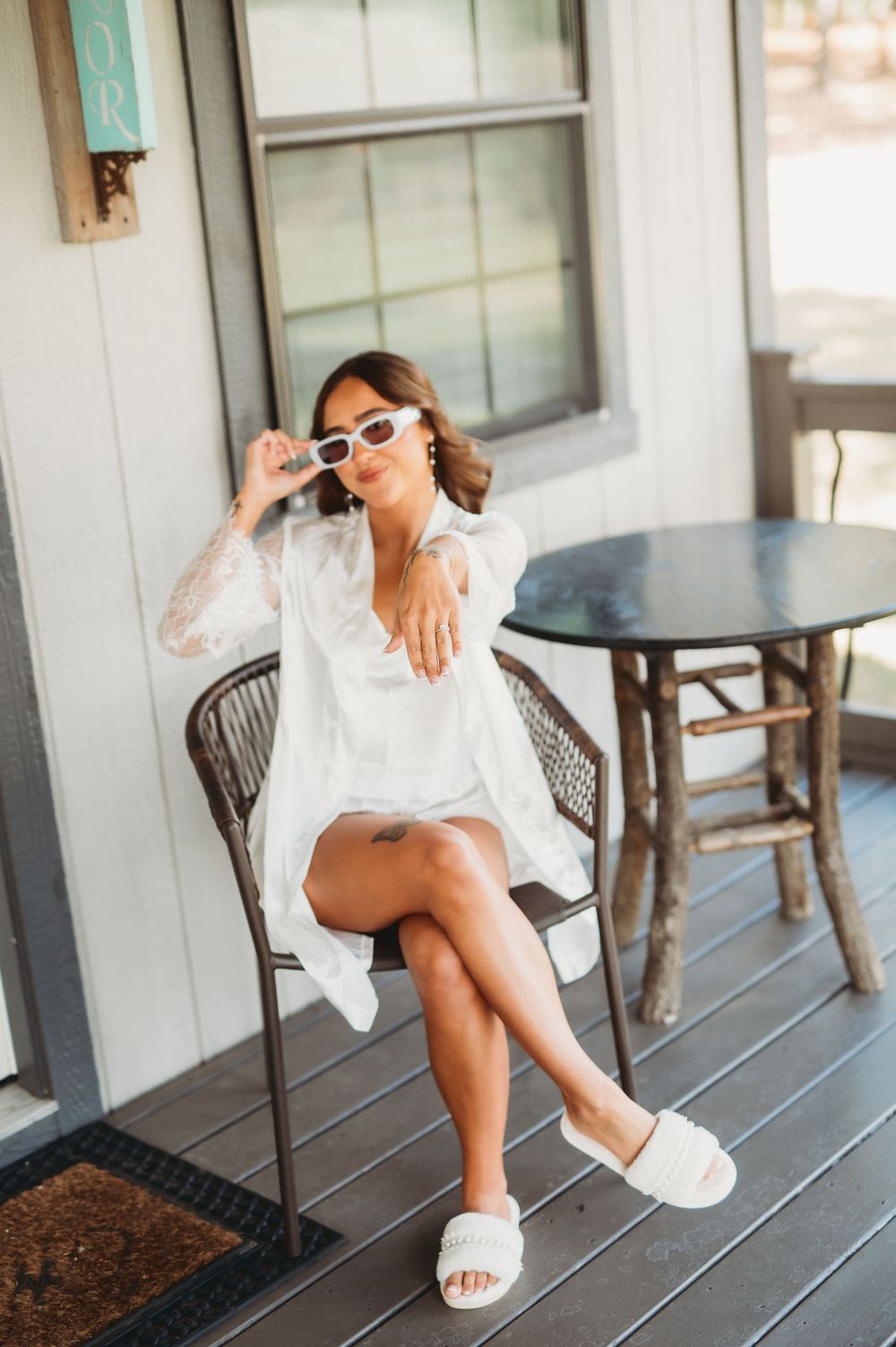 Stylish white summer outfit with slides photographed on a rustic porch with wooden chairs and table.