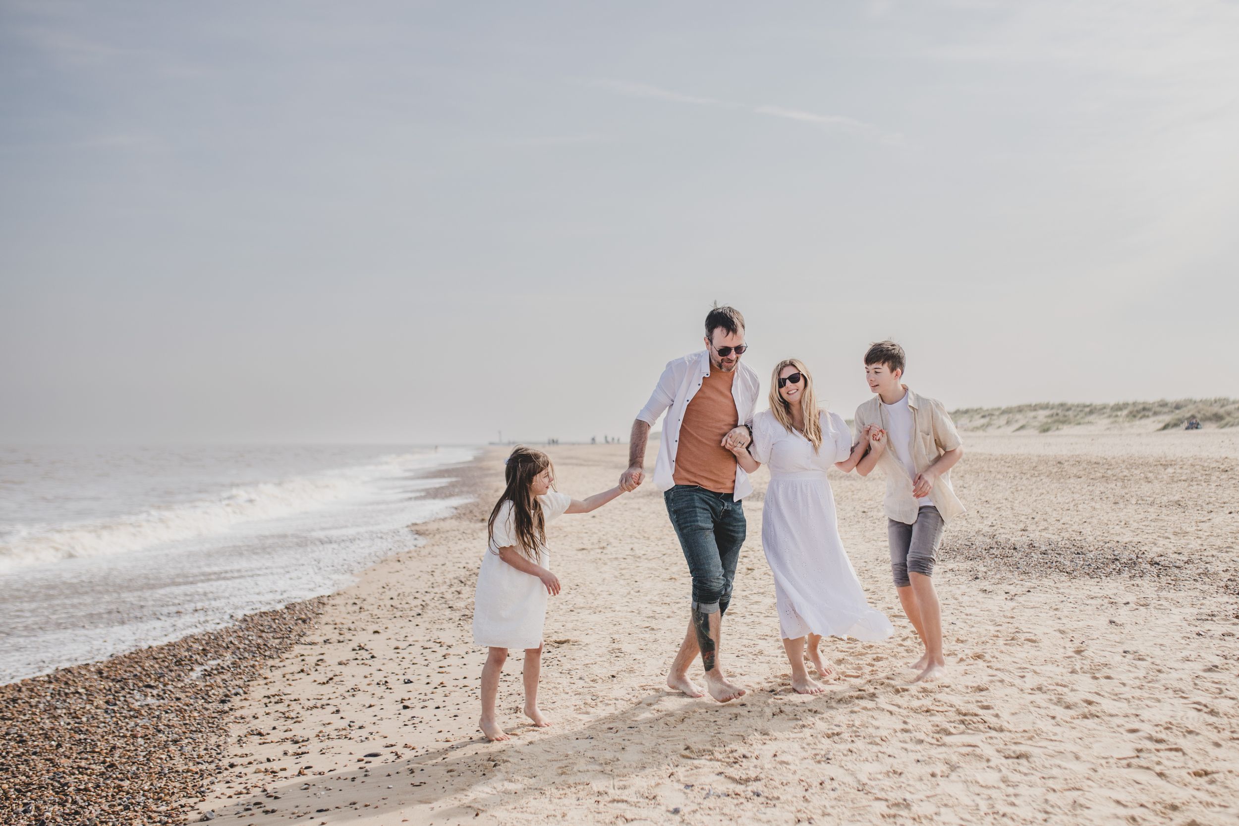 Family walking hand in hand along a sunny beach shoreline.