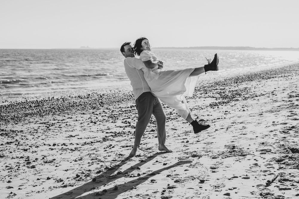 A joyful couple twirls together on a beach during a romantic black and white photoshoot.