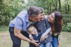 A joyful family sharing a candid moment of laughter together in a lush green forest setting.