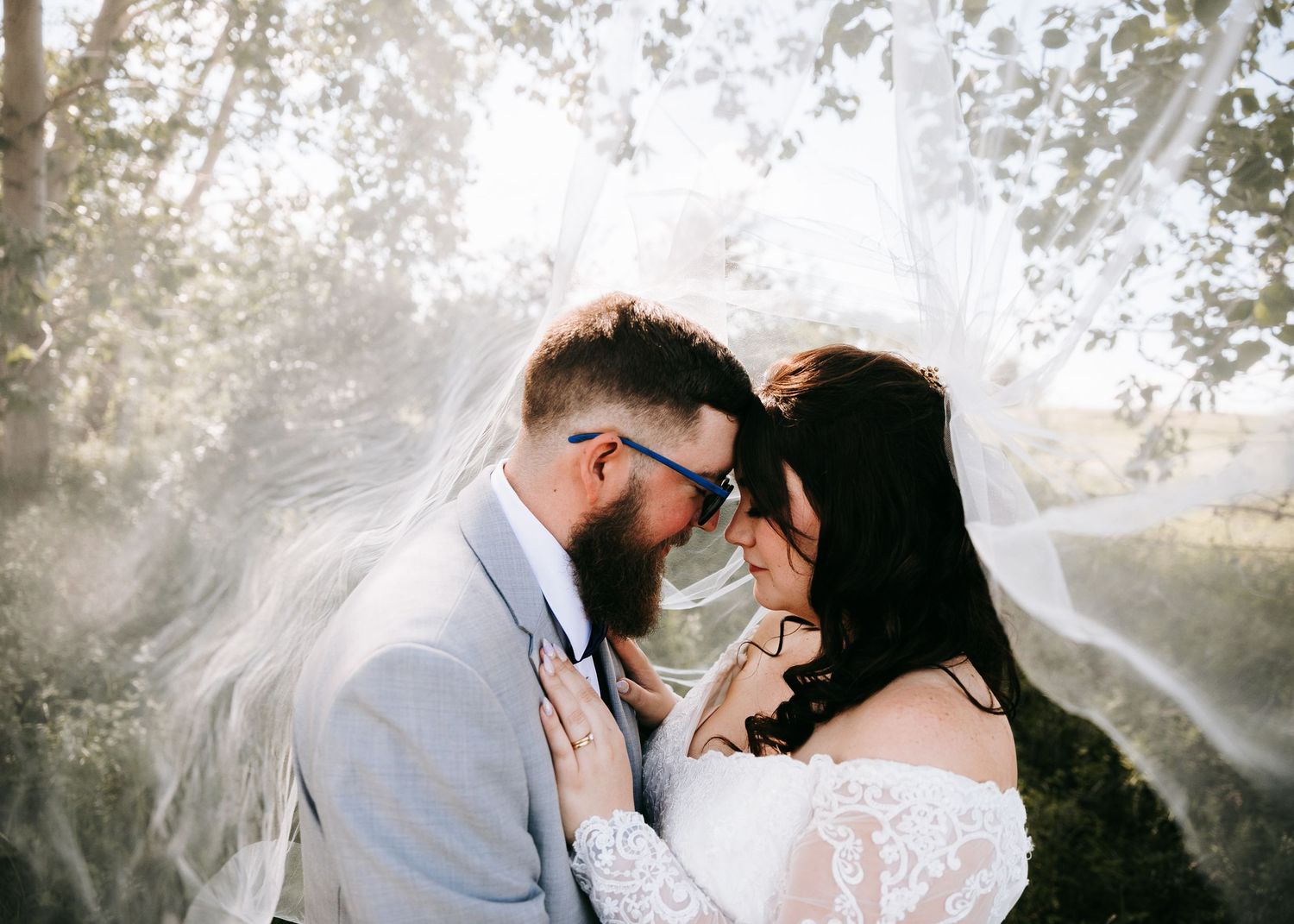 Romantic bride and groom sharing an intimate moment under a flowing wedding veil outdoors.