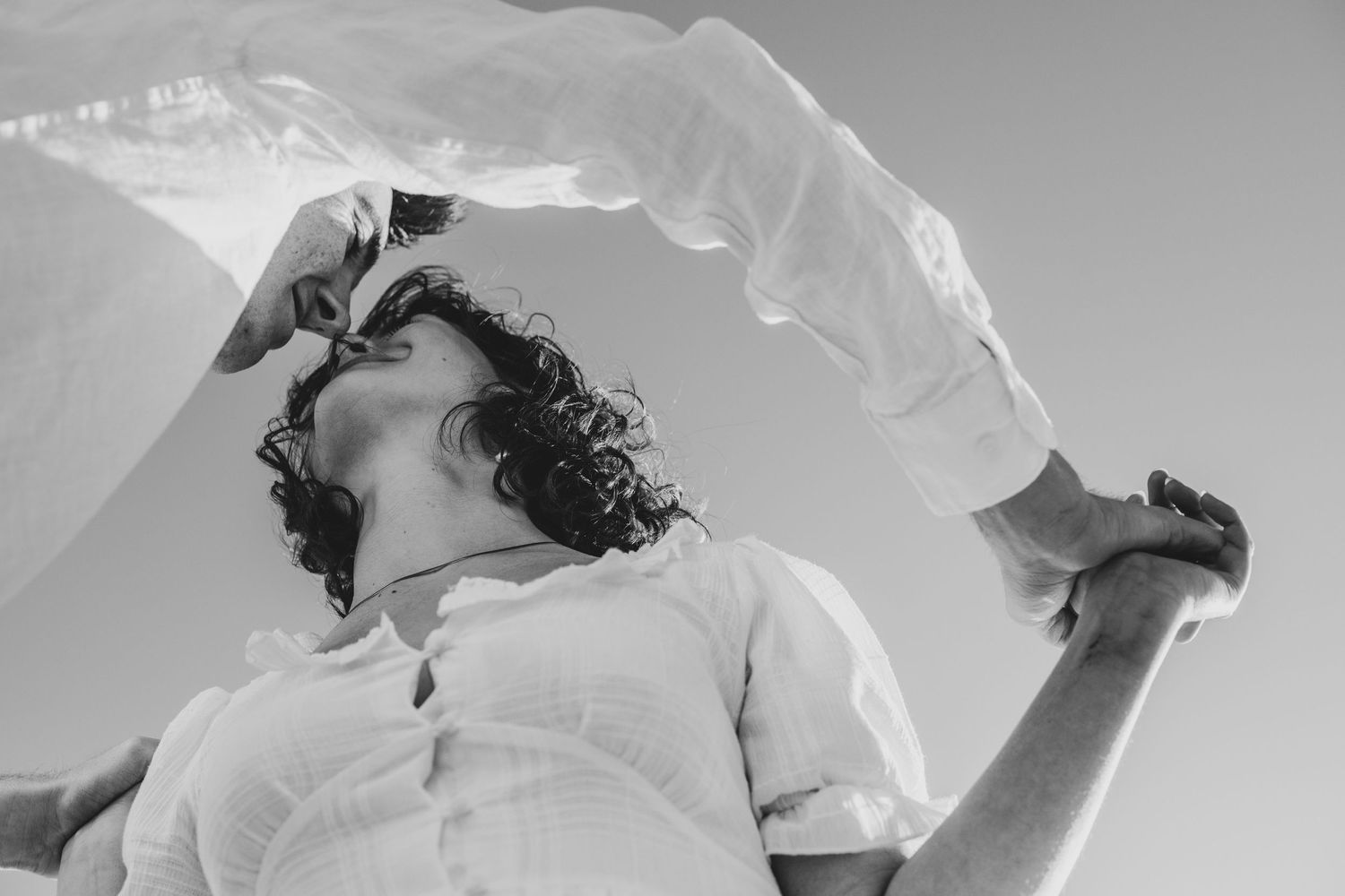 A joyful couple twirls together on a beach during a romantic black and white photoshoot.