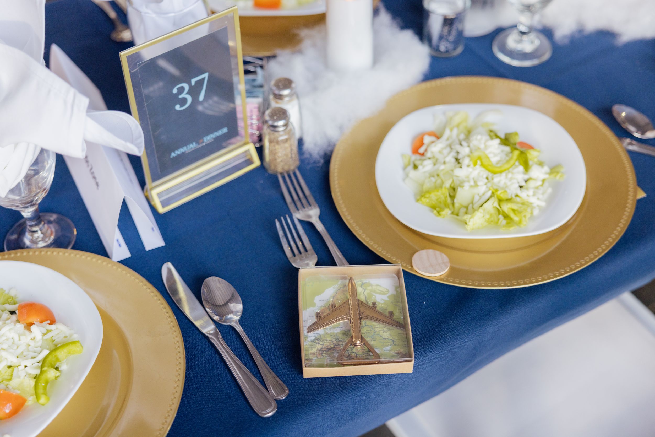 Place setting with gold charger plate and salad on navy blue tablecloth.