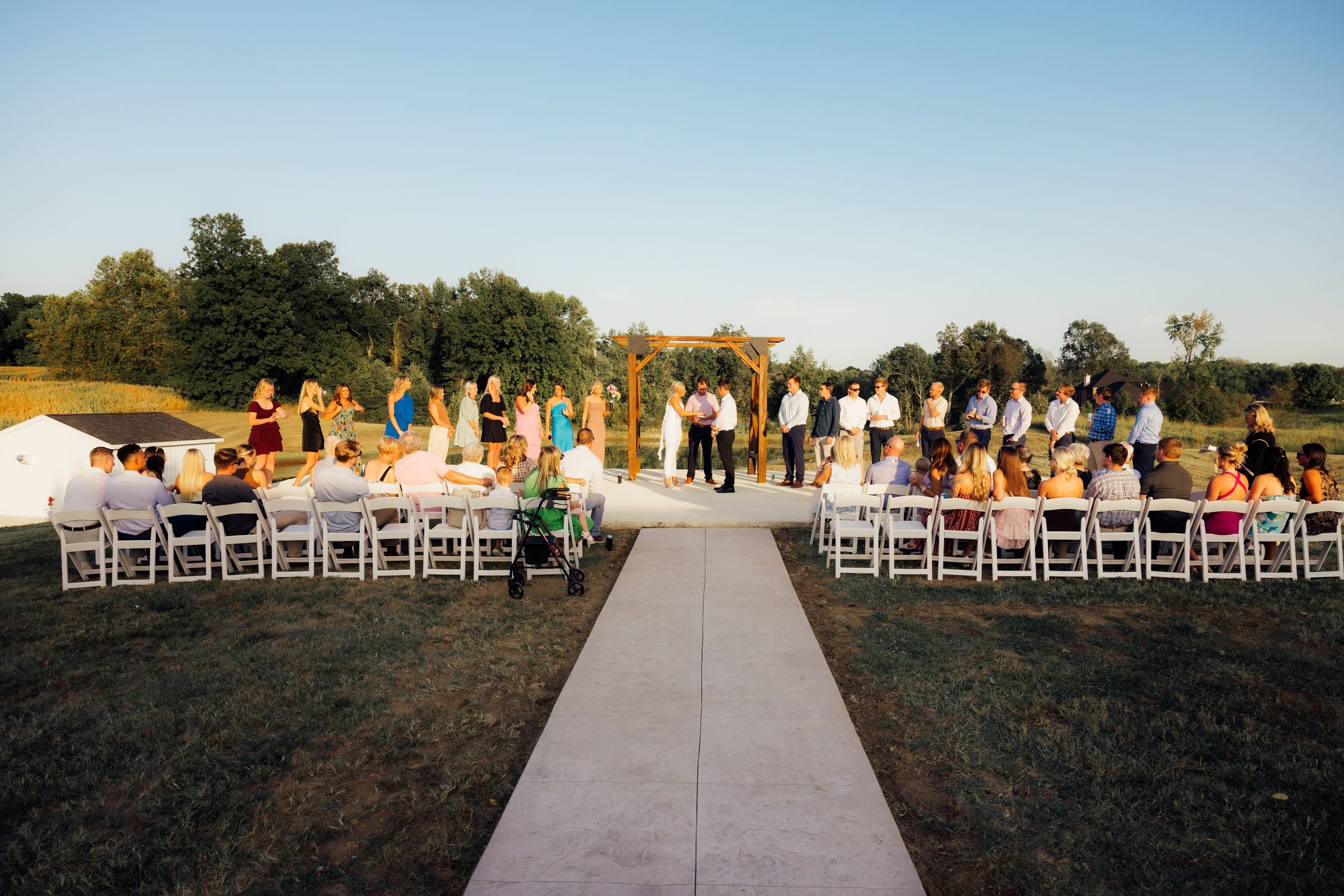 Outdoor wedding ceremony setup with white chairs and aisle runner in natural setting.