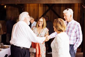 Guests enjoying conversation at a rustic barn wedding reception with wooden walls and white decor.