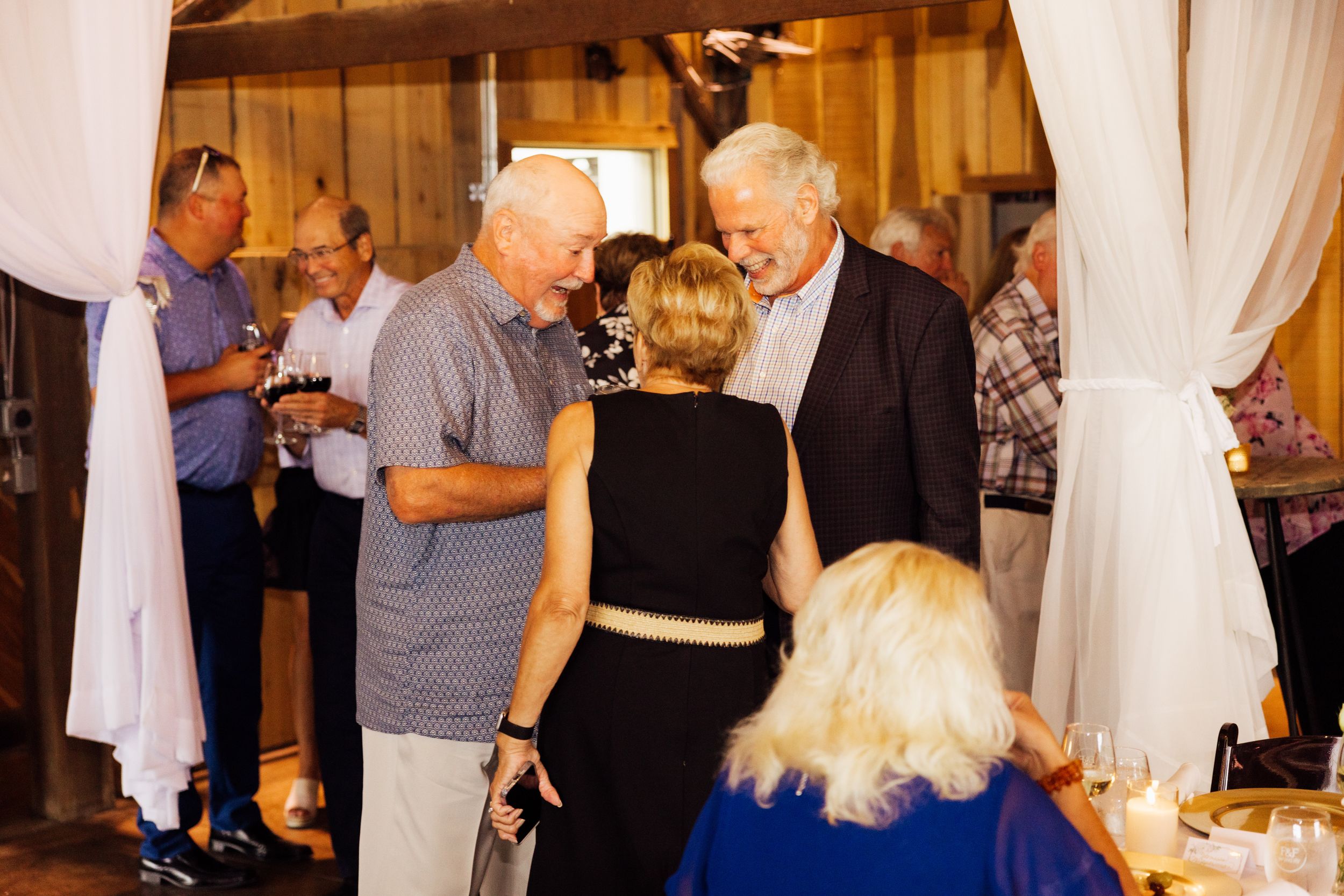 Anniversary dinner socializing near white curtains at rustic indoor venue.