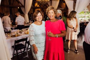 Two guests in elegant dresses, one blue lace and one red, pose together at event.