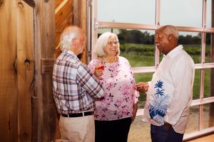 Three guests chatting near wooden walls and windows at social gathering.