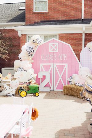 Pink barn-themed party backdrop with hay bales and balloon decorations.