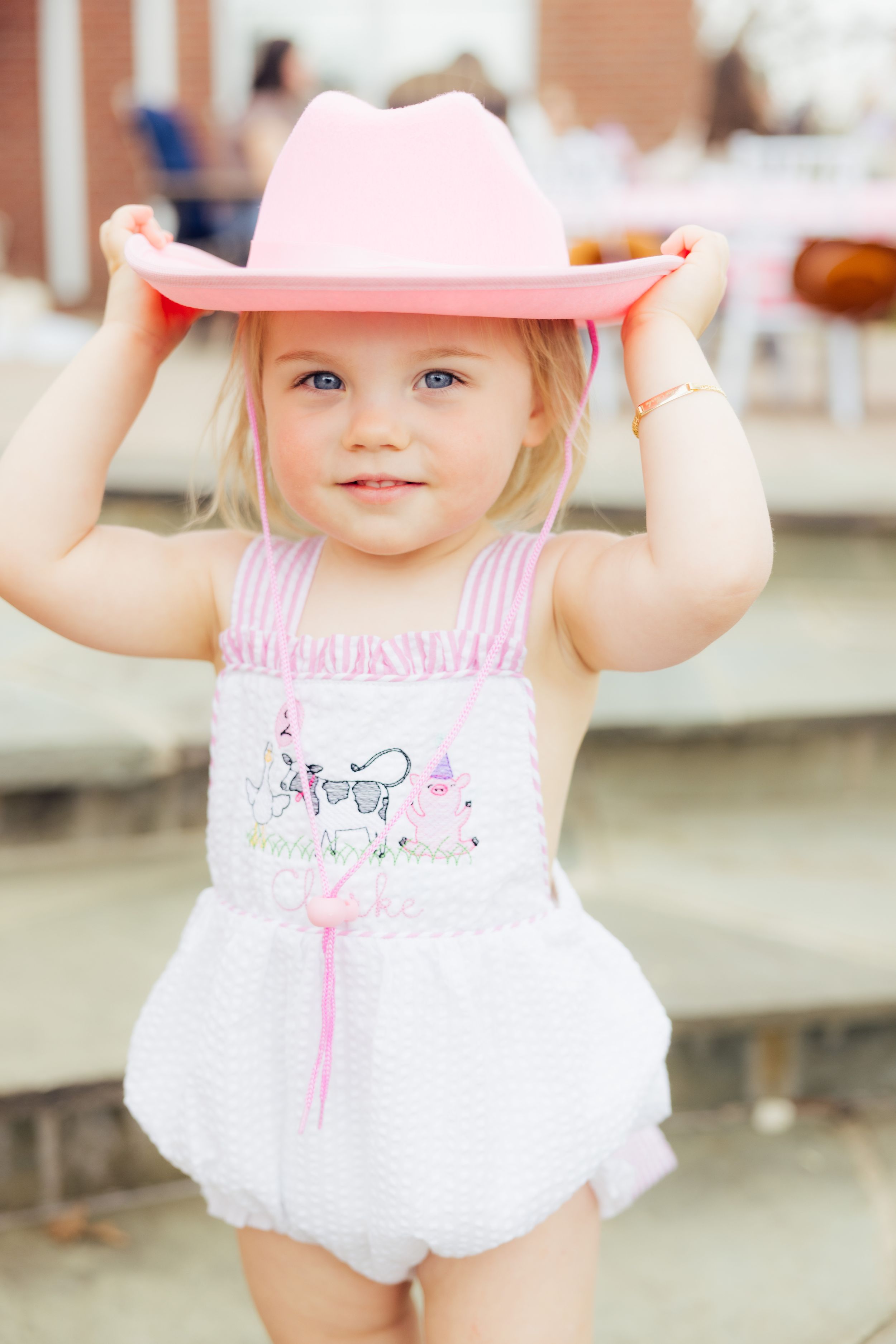 Baby wearing pink and white outfit with matching hat at farm-themed birthday party.