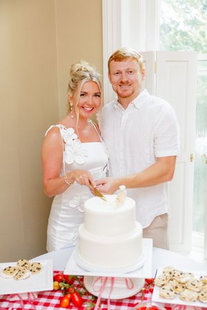 Wedding cake cutting moment with couple in matching white outfits.