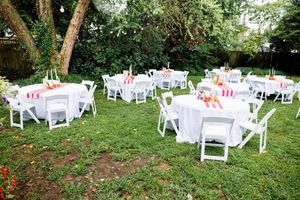 Outdoor party setup with white chairs and tables arranged on a grassy lawn.