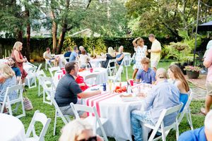Outdoor wedding reception setup with white chairs and red accents in a garden setting.
