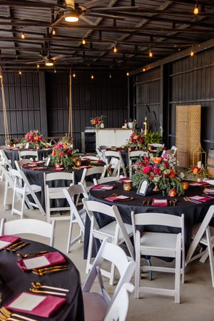 Elegant wedding rehearsal dinner setup with black tablecloths and colorful floral centerpieces.