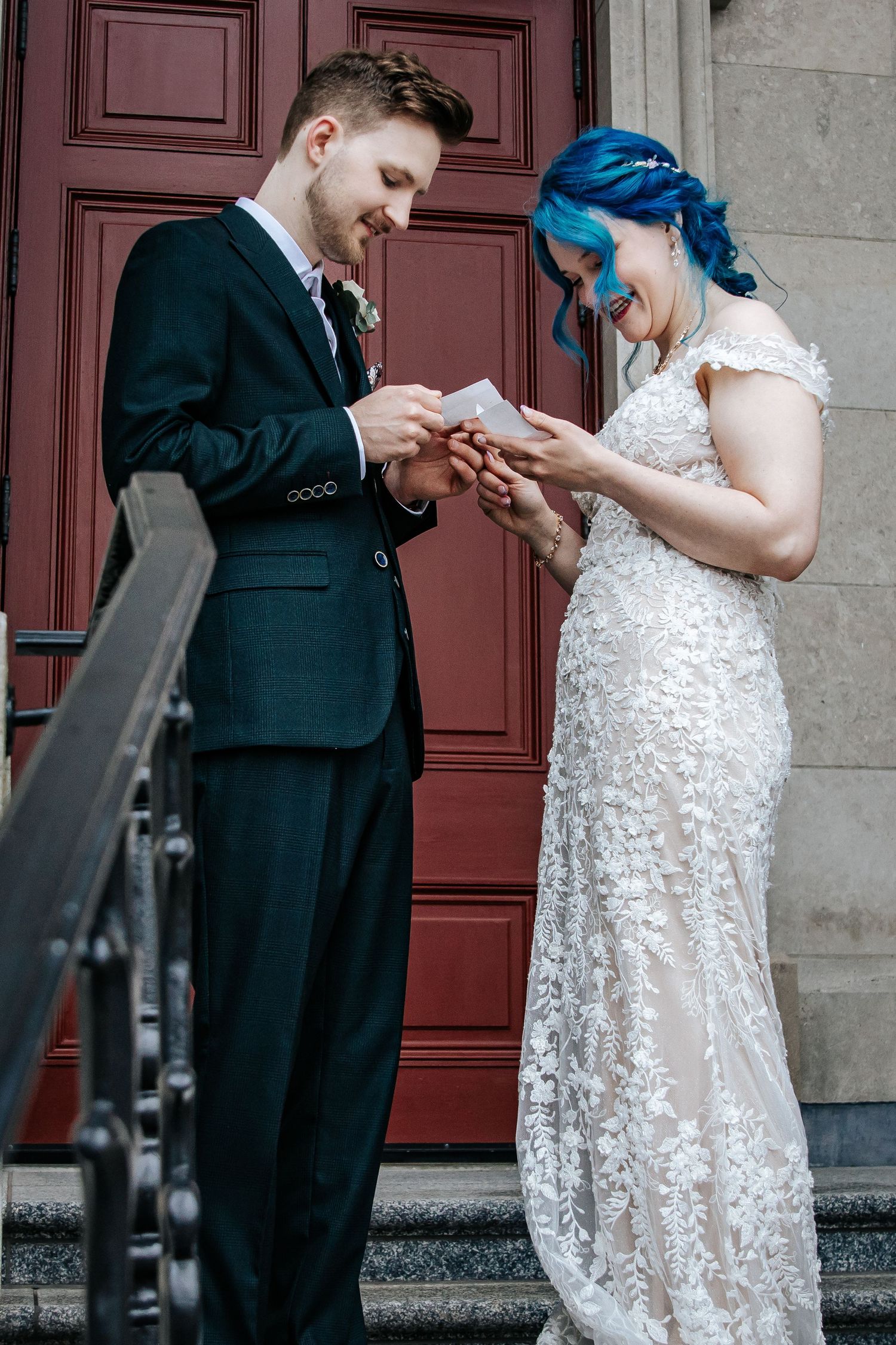 A blue haired bride in a lace dress and a groom wearing a black suit read their vows privately to each other.