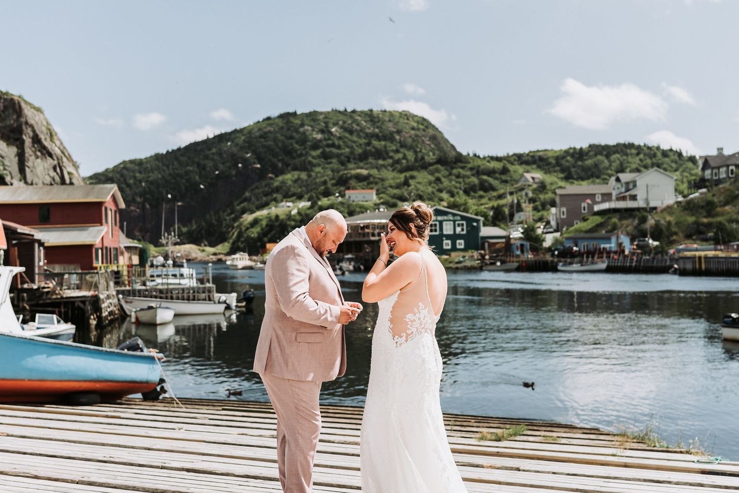 A couple shares a tender moment on a scenic dock by a marina with boats and hills in the background.