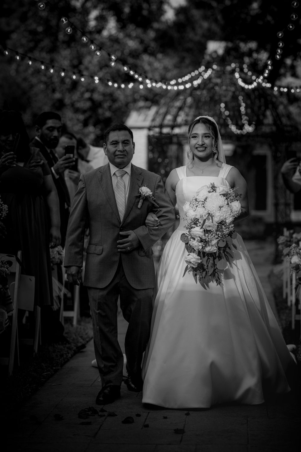 A romantic outdoor wedding ceremony with string lights overhead and guests watching the couple exchange vows.