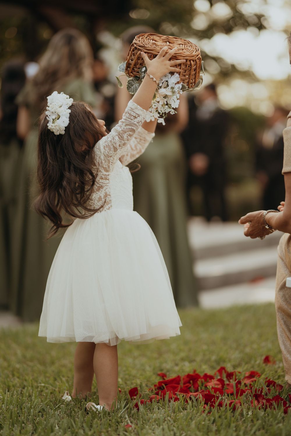 Little flower girls in white dresses playing near red flowers on a grassy lawn.