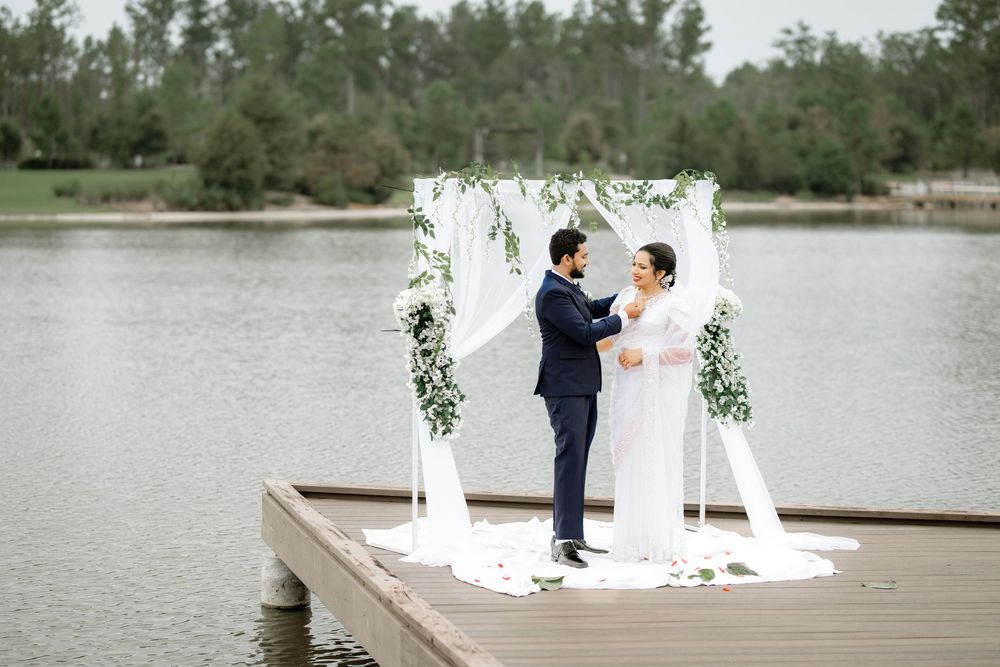 Elegant lakeside wedding ceremony setup with white floral arch and water views.