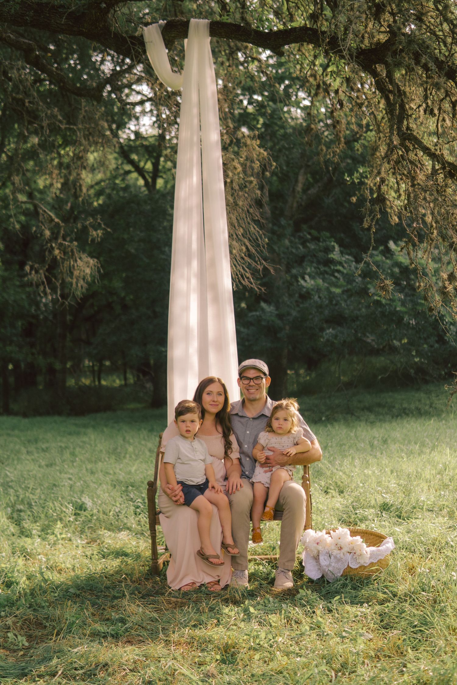 A fabric-draped tree in a lush green setting with flowers frames a local Austin family during golden hour.