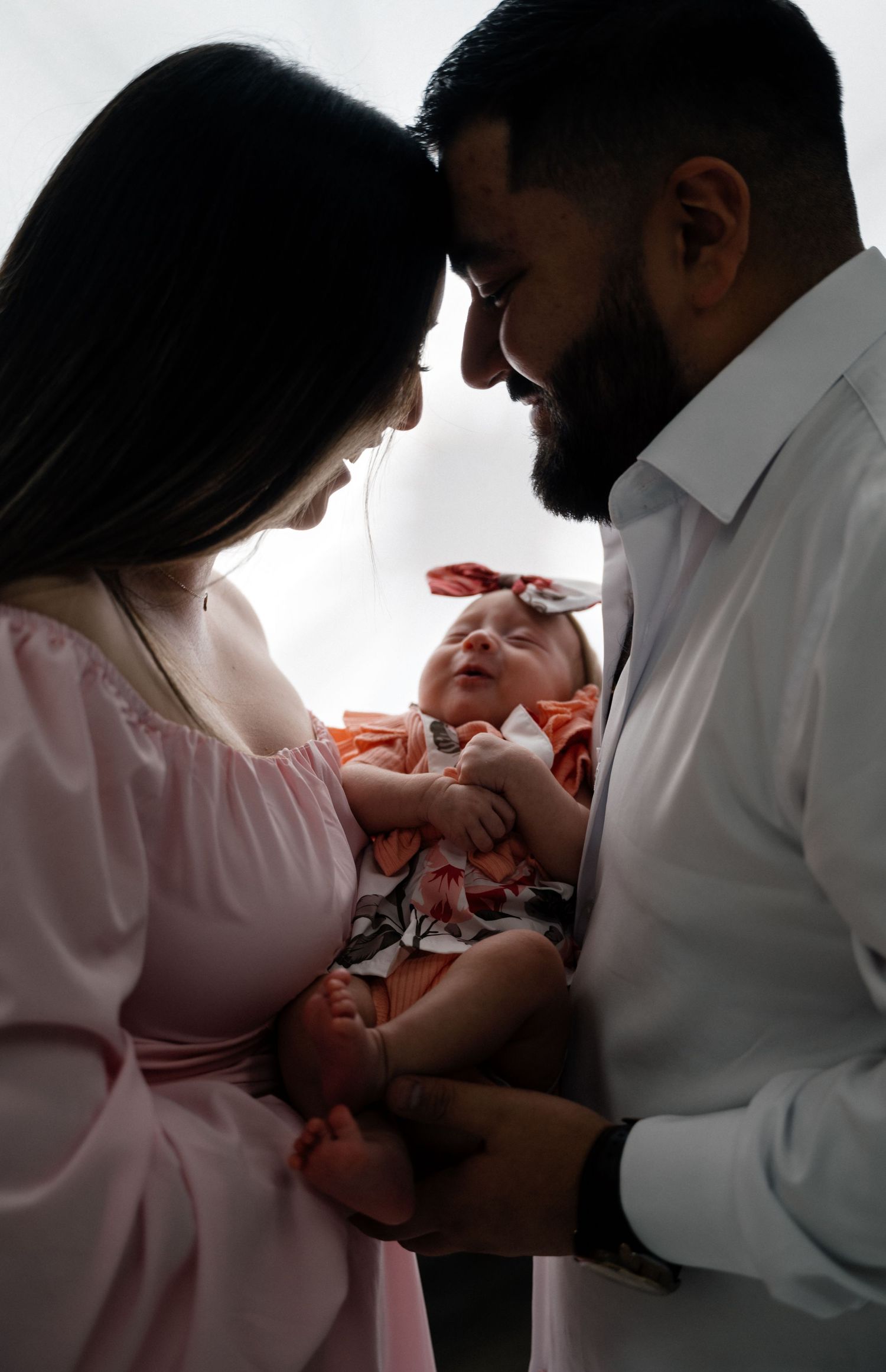 Parents sharing intimate moment with newborn baby in backlit portrait.
