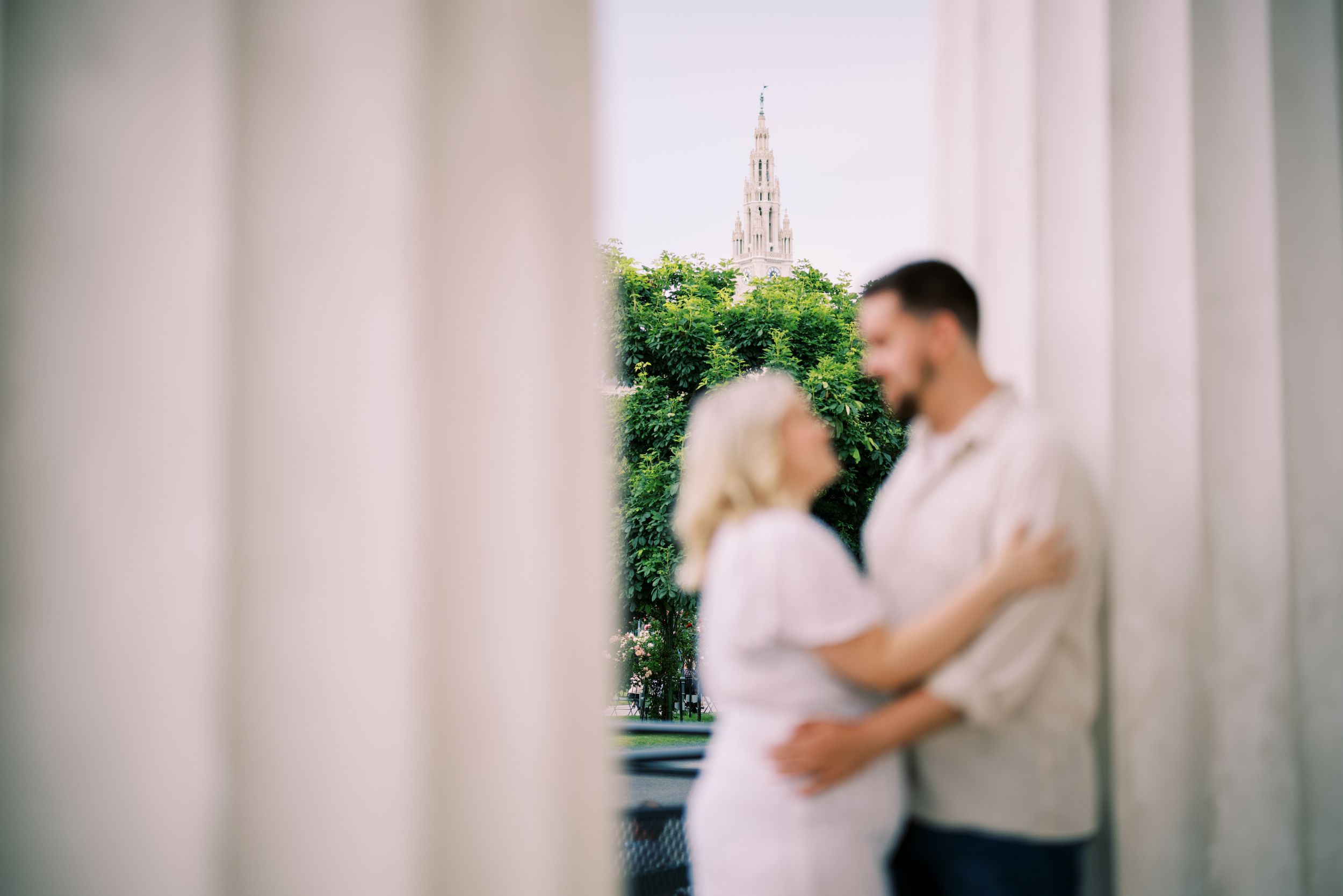 A romantic couple embraces in front of a garden archway in a soft focus photograph.