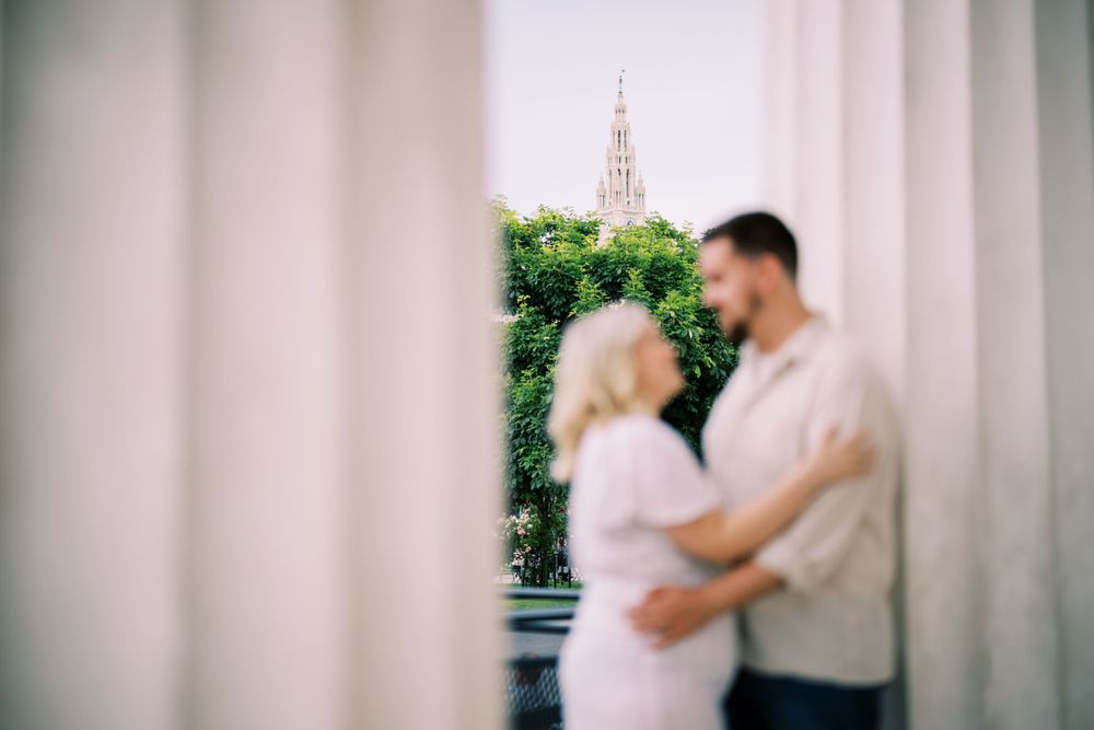 A romantic couple embraces in front of a garden archway in a soft focus photograph.