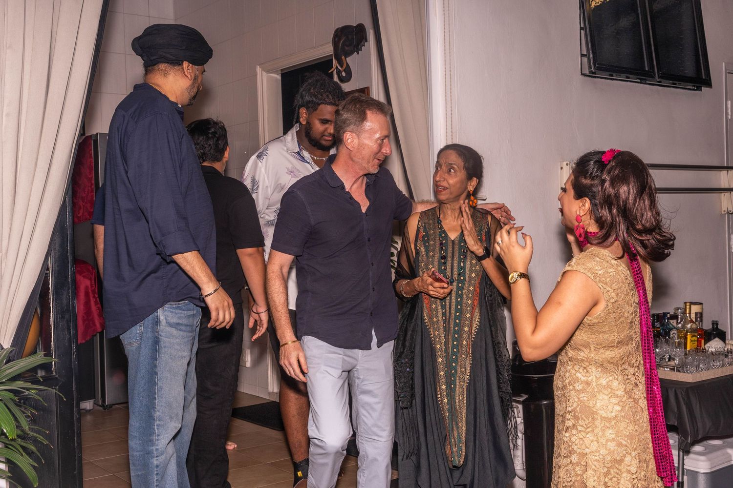 Party guests mingling and chatting in casual attire at an indoor social gathering.