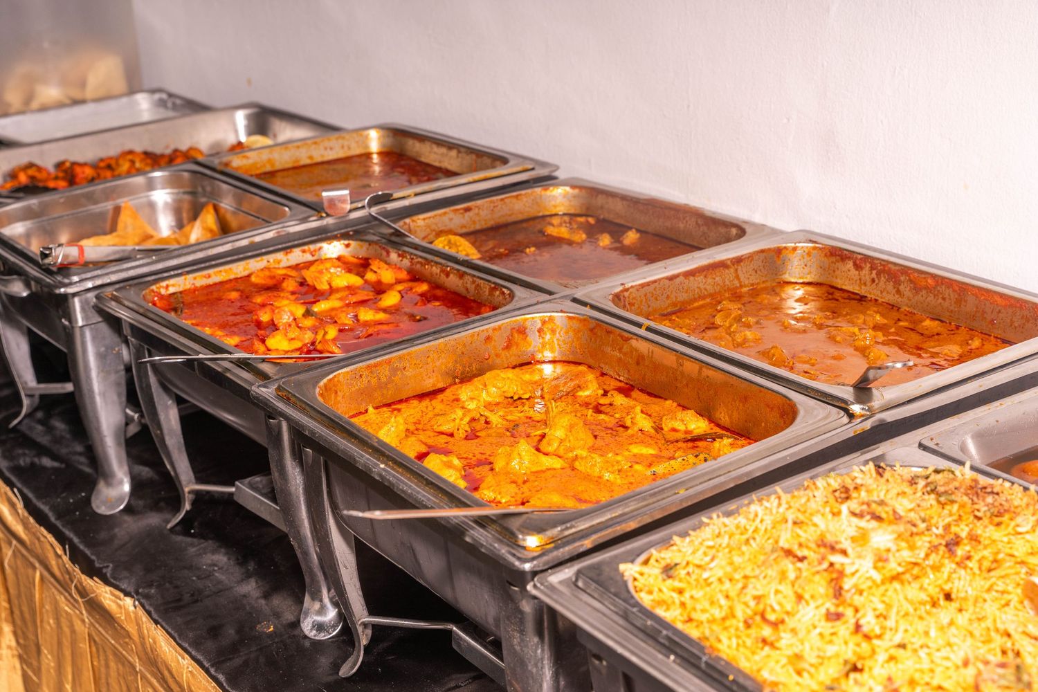 Buffet line of Indian curry dishes in metal chafing dishes with warming flames underneath.