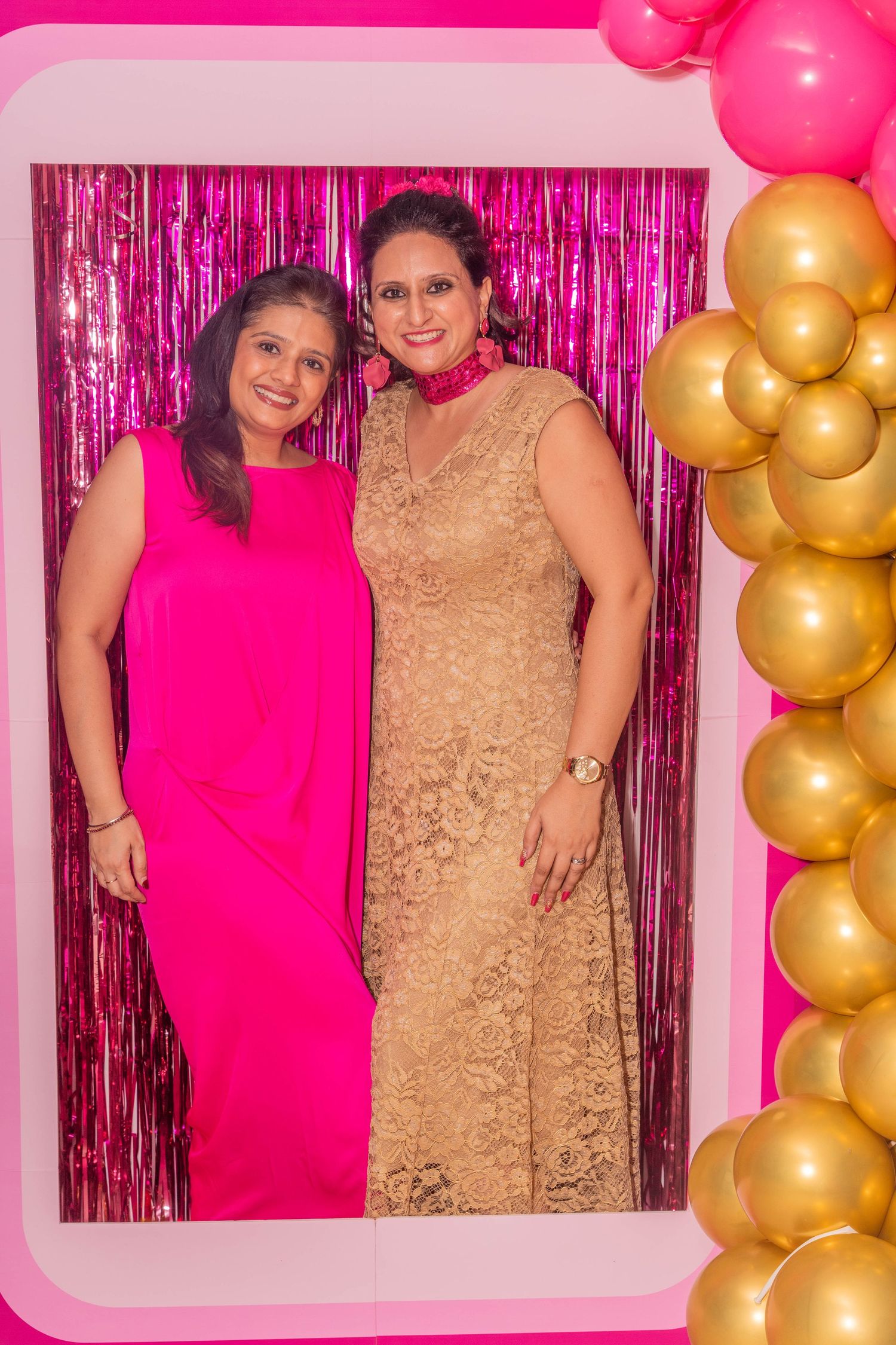 Festive photo booth setup with pink metallic backdrop and gold balloon decorations.