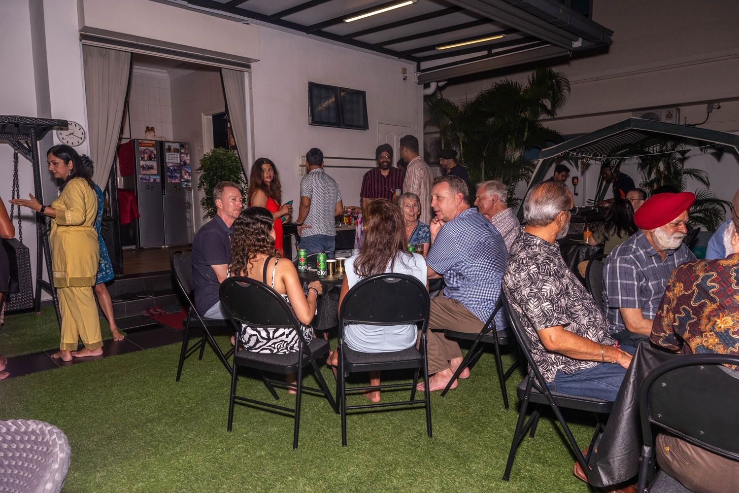 Party guests seated in chairs arranged in circle for social gathering on indoor patio.