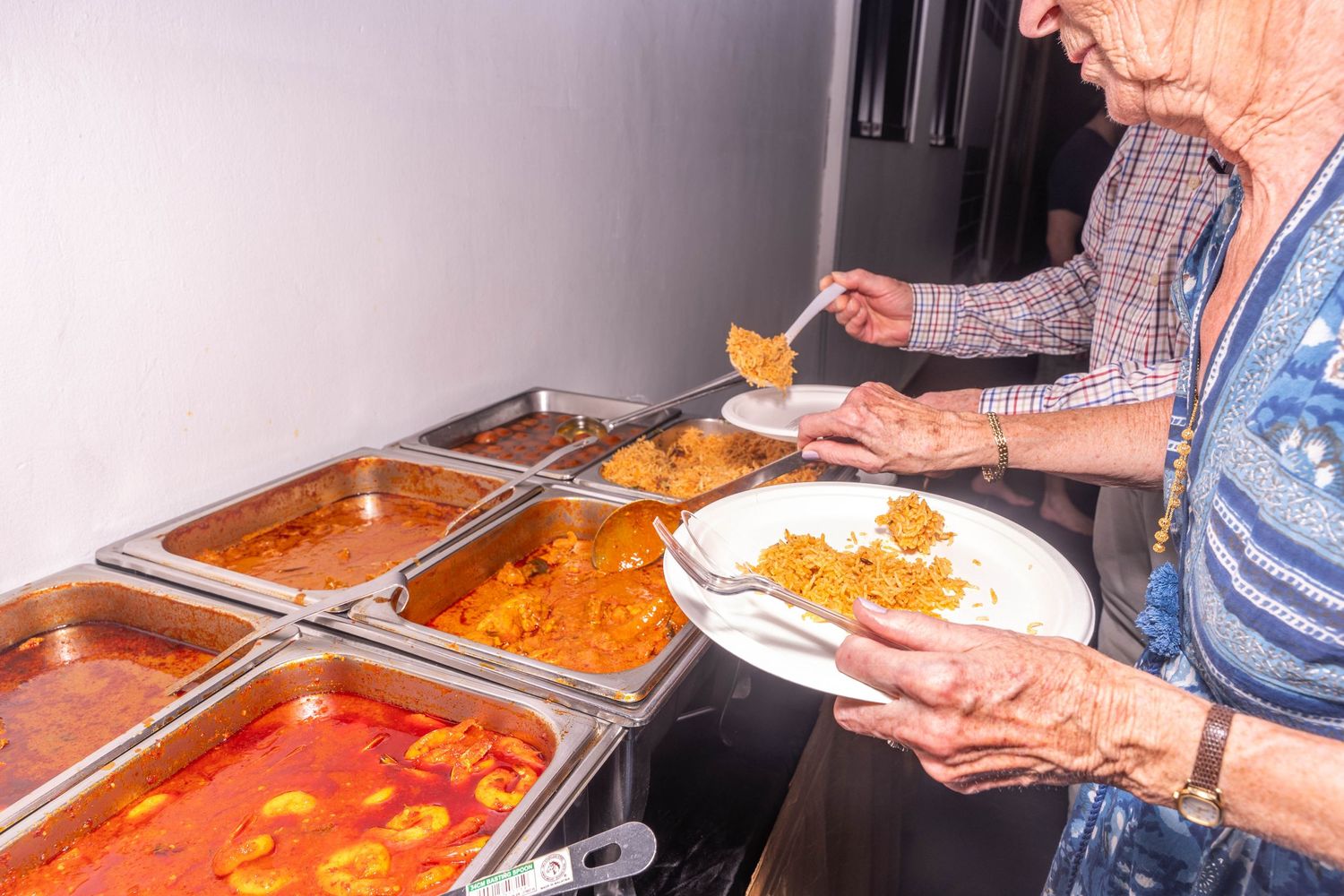 Guests serving themselves from Indian food buffet line with various curry dishes.