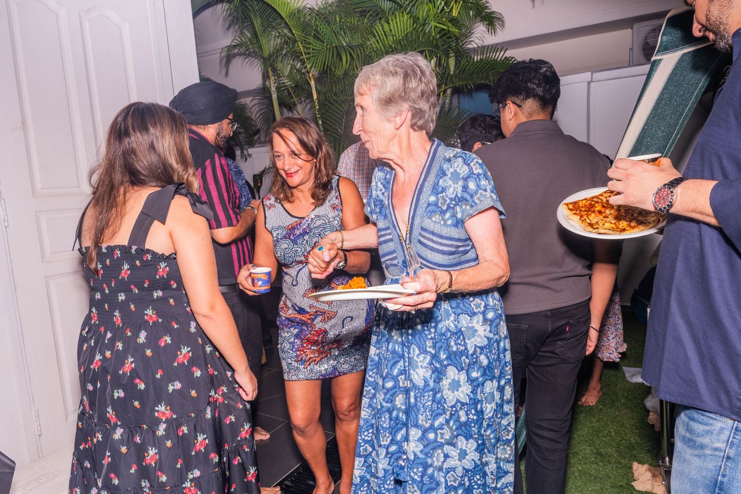 A group of guests mingling at an outdoor party while holding plates of food and drinks.