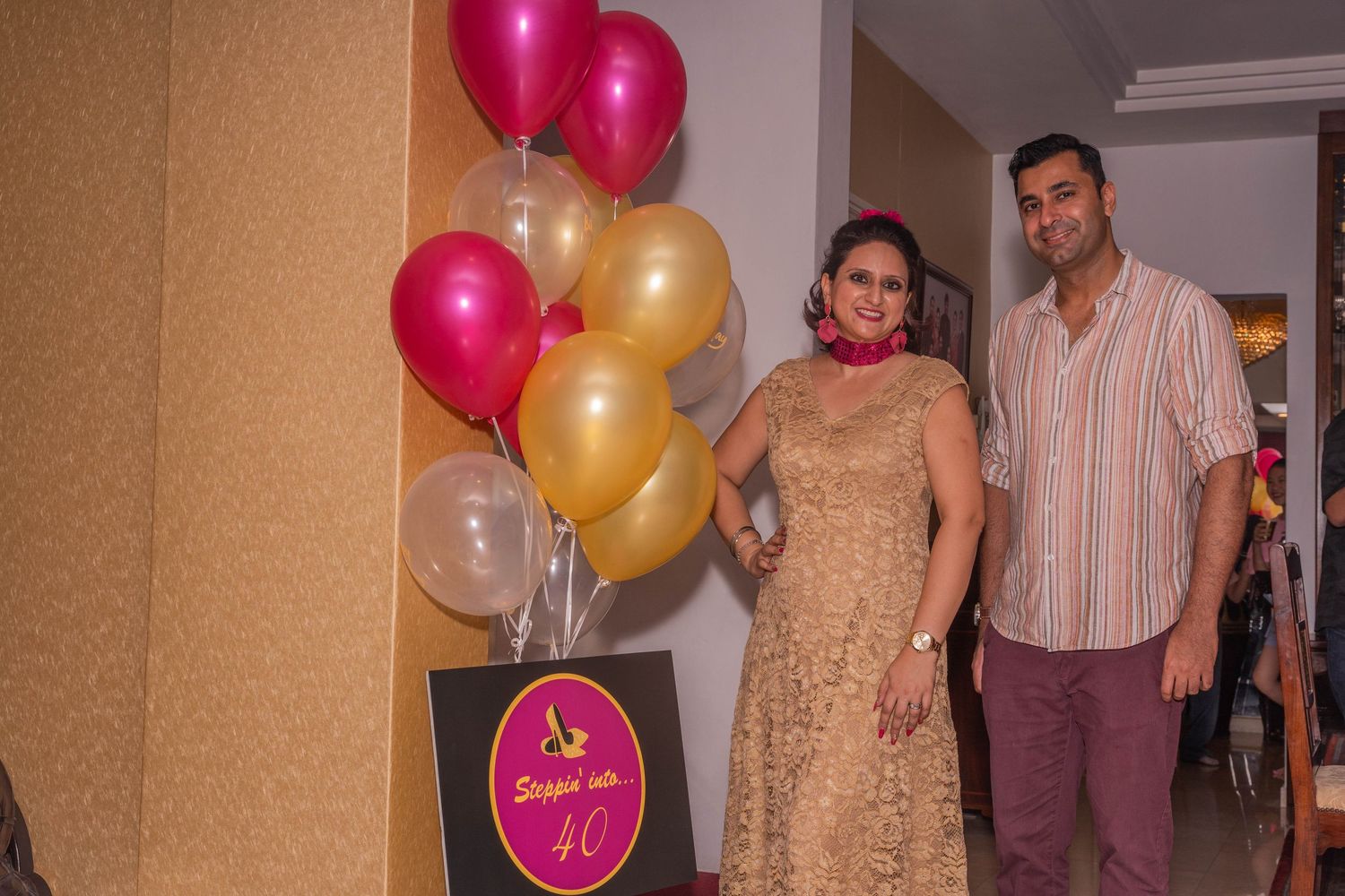 A couple standing next to pink and gold balloons at a celebration event.