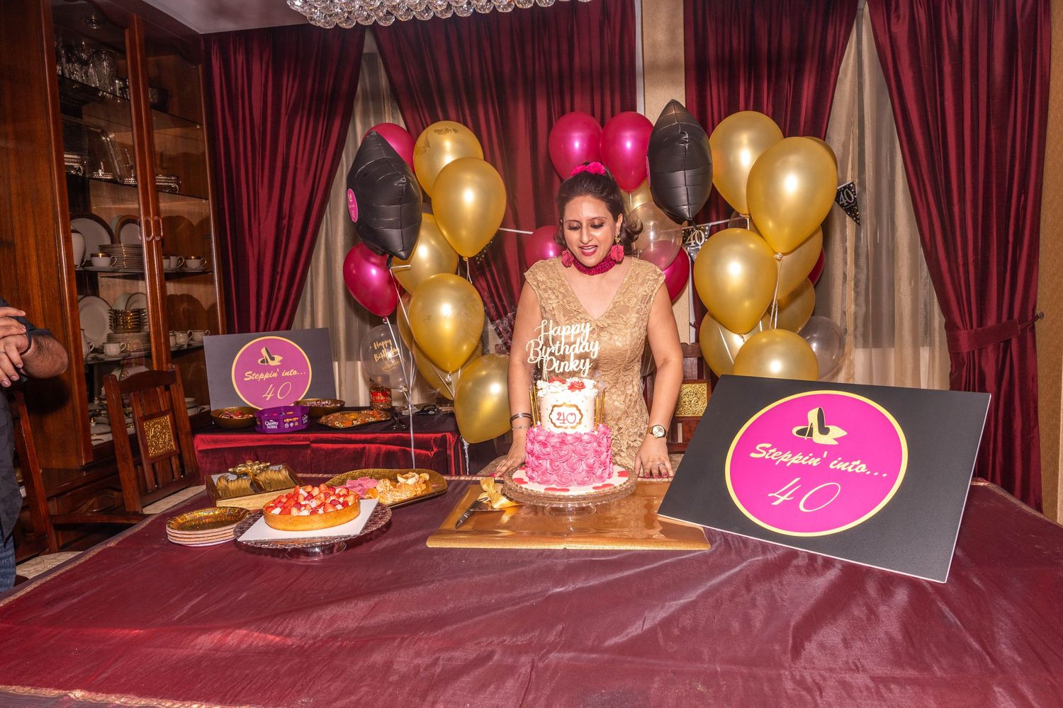 Birthday celebration setup with pink cake, gold and pink balloons, and decorative signs.