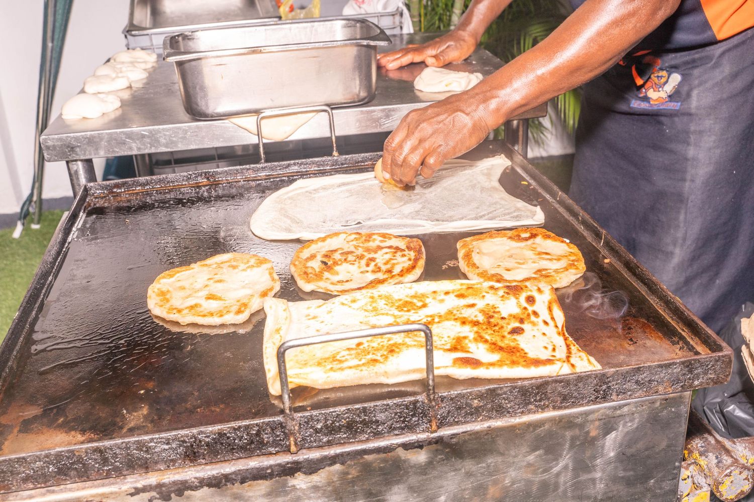 Chef cooking multiple flatbreads on large outdoor grill.