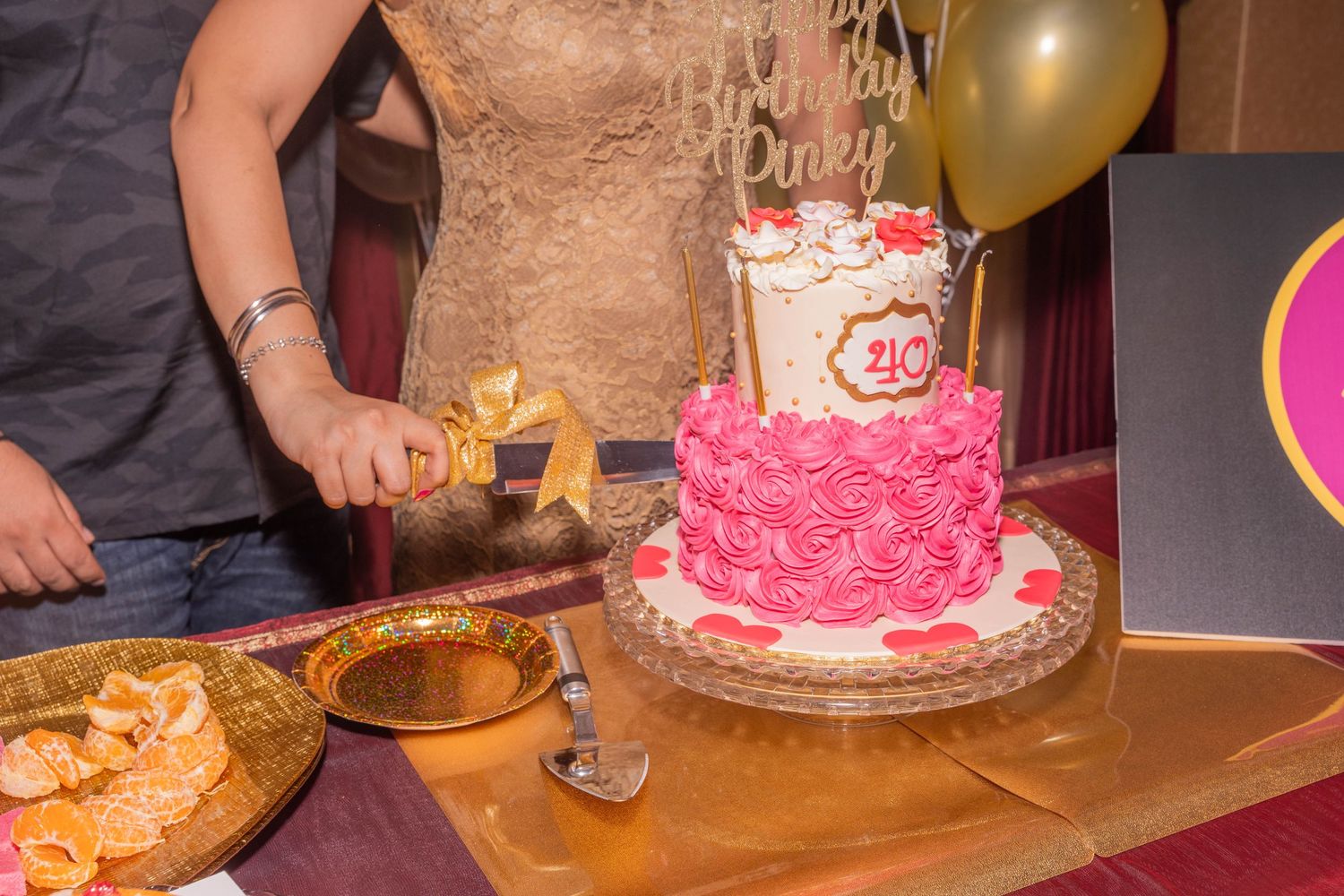 Close-up of a pink tiered birthday cake being cut on a decorated table.