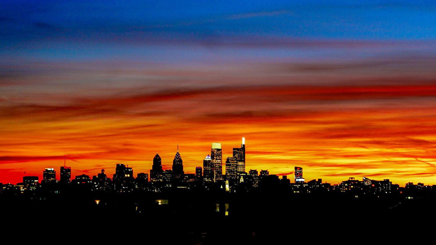 Philadelphia skyline silhouetted against a dramatic orange and red sunset sky.