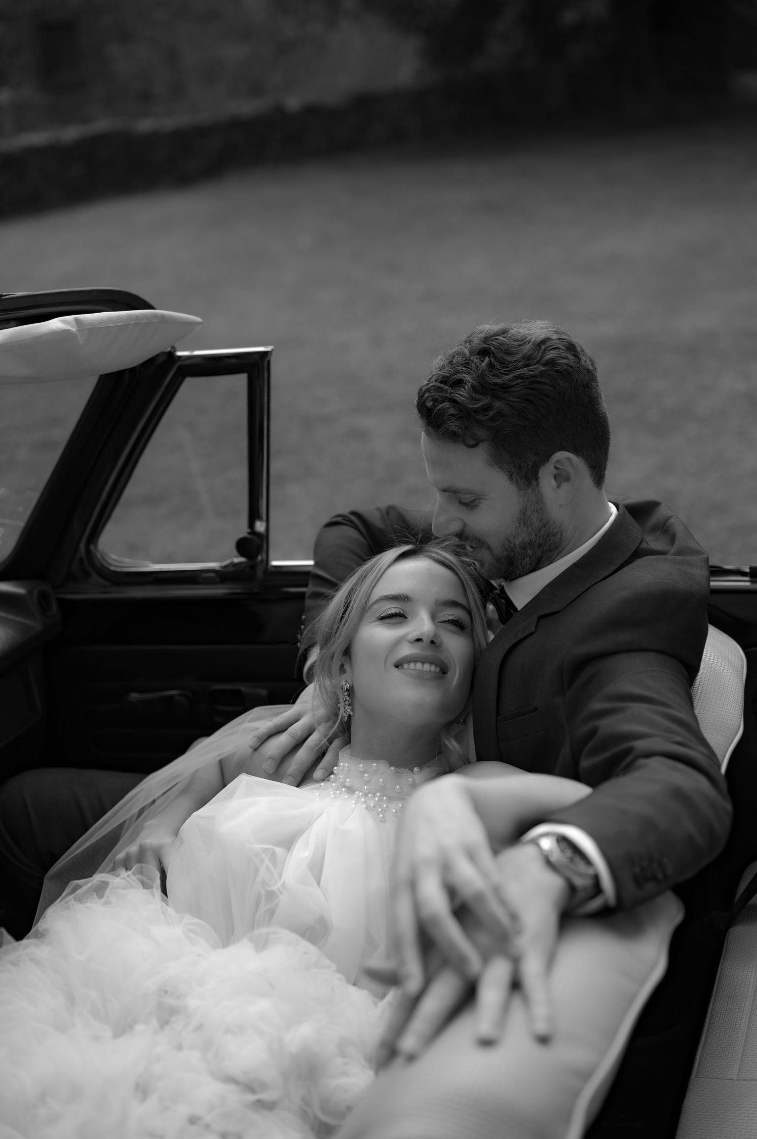 Romantic wedding scene with couple in vintage car surrounded by flowing white dress.